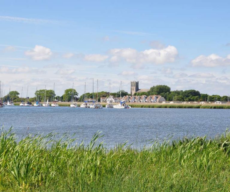 Peaceful view of Christchurch Harbour with sailboats and distant buildings.