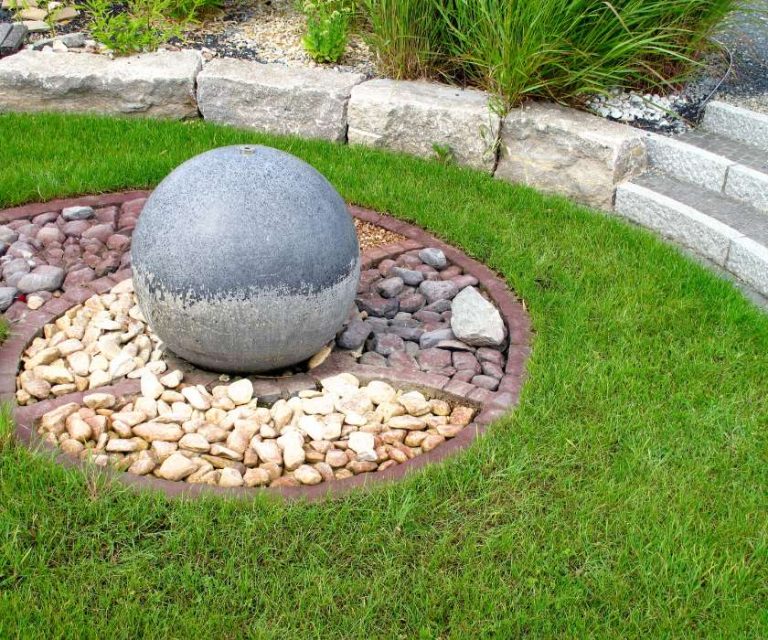 Circular stone garden feature with a central spherical ornament, surrounded by pebbles and green grass in Holbury