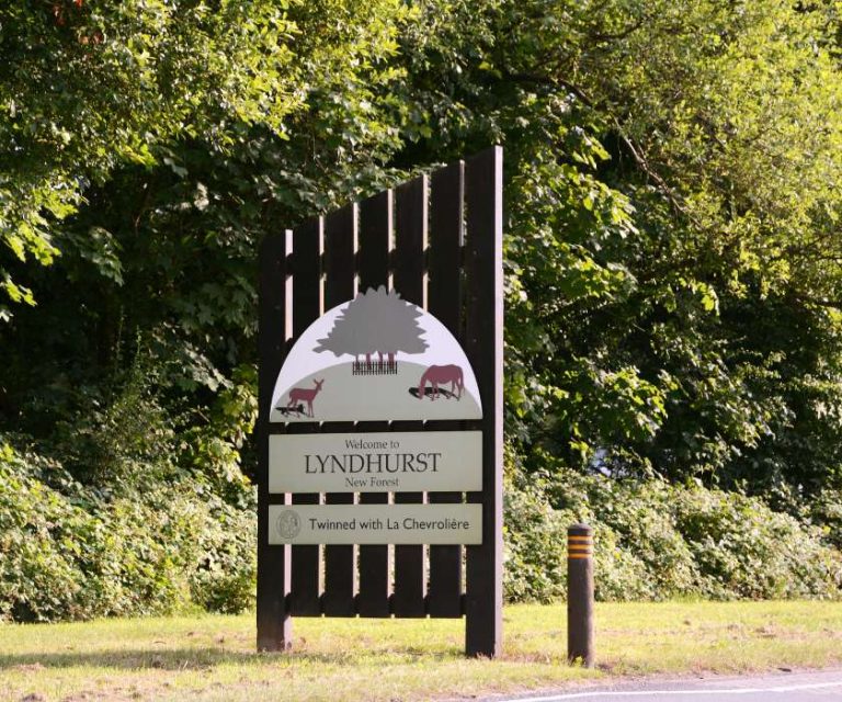 Welcome sign for Lyndhurst in the New Forest, surrounded by greenery.