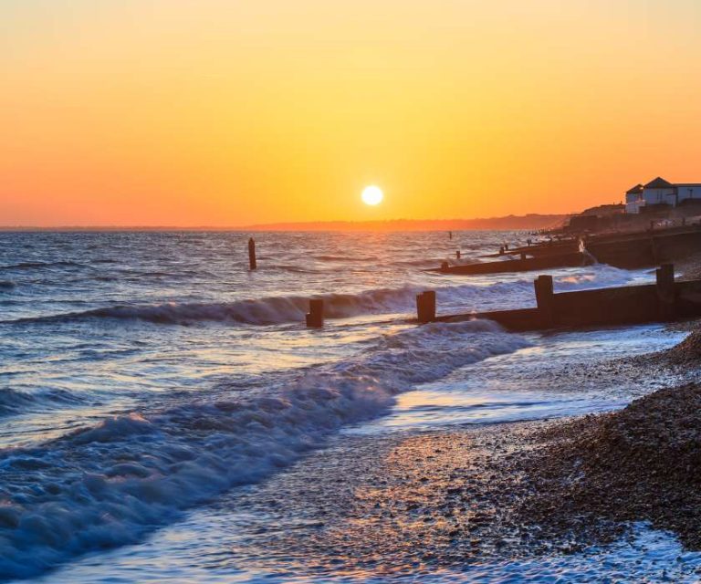 Golden sunset over the waves at Milford-on-Sea, with coastal defences visible along the shore.