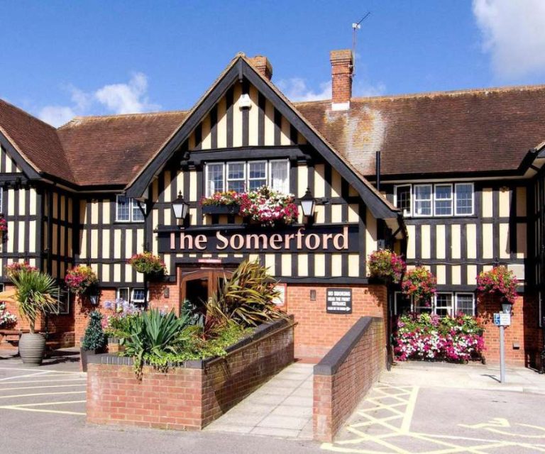 The Somerford Inn with classic black and white Tudor-style architecture and colourful flower baskets.