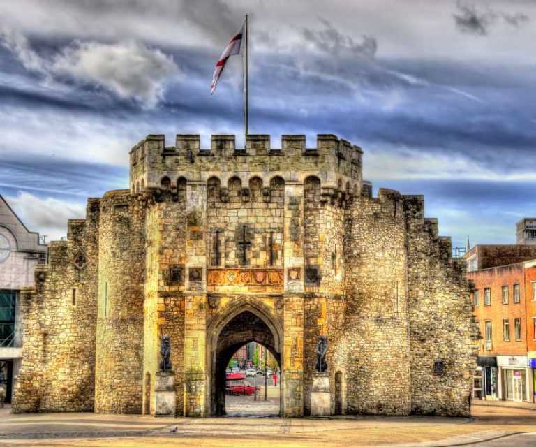 Medieval stone gate in Southampton, featuring an archway and the English flag flying above.