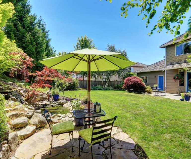 Charming garden in Sway featuring a patio table with a green umbrella, lush lawn, and colourful plants.